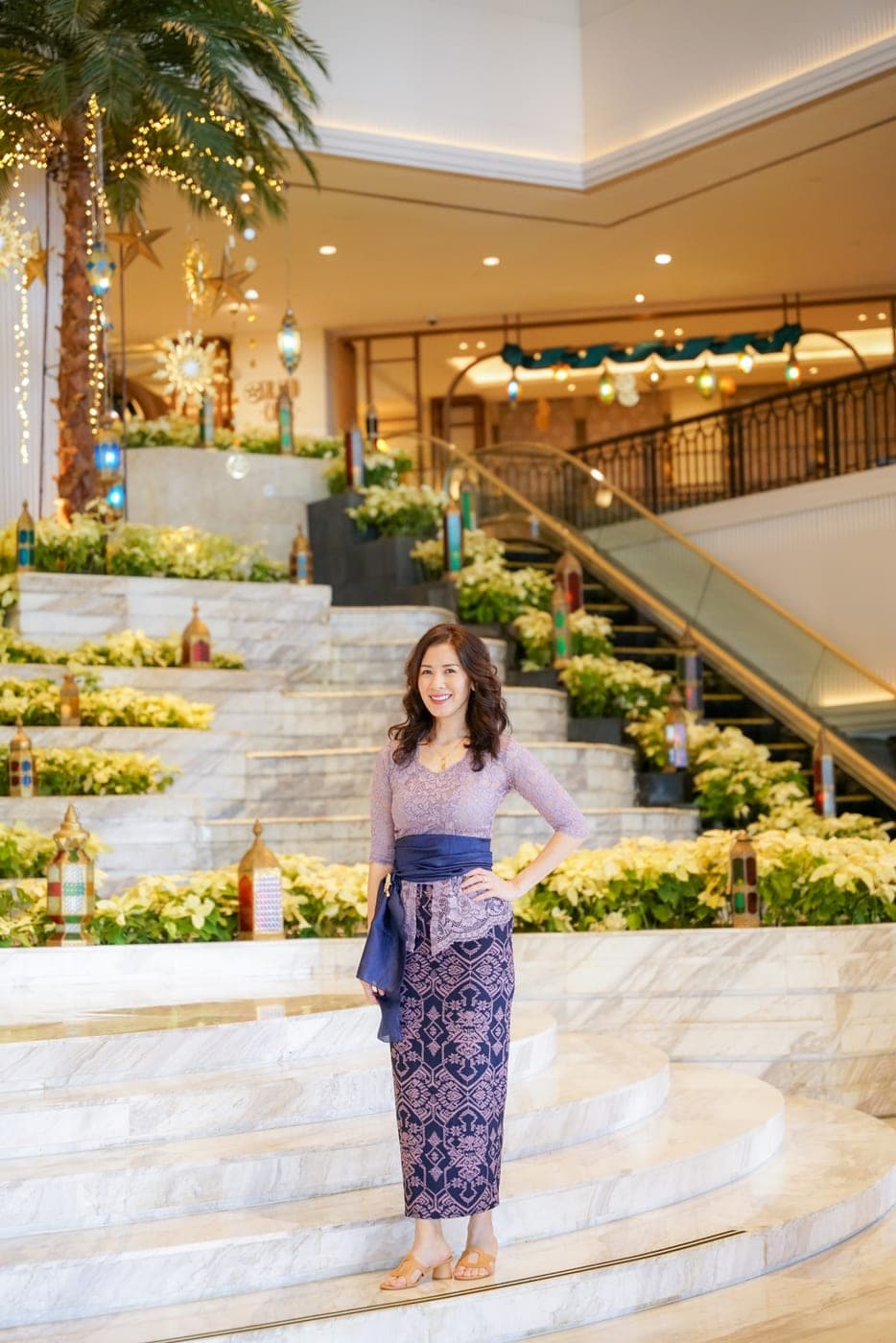 Woman in a purple kebaya posing on stairs with floral decorations