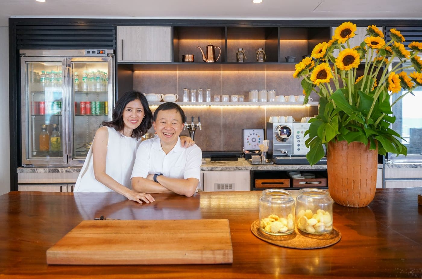 Couple in white posing at a wooden counter beside sunflowers