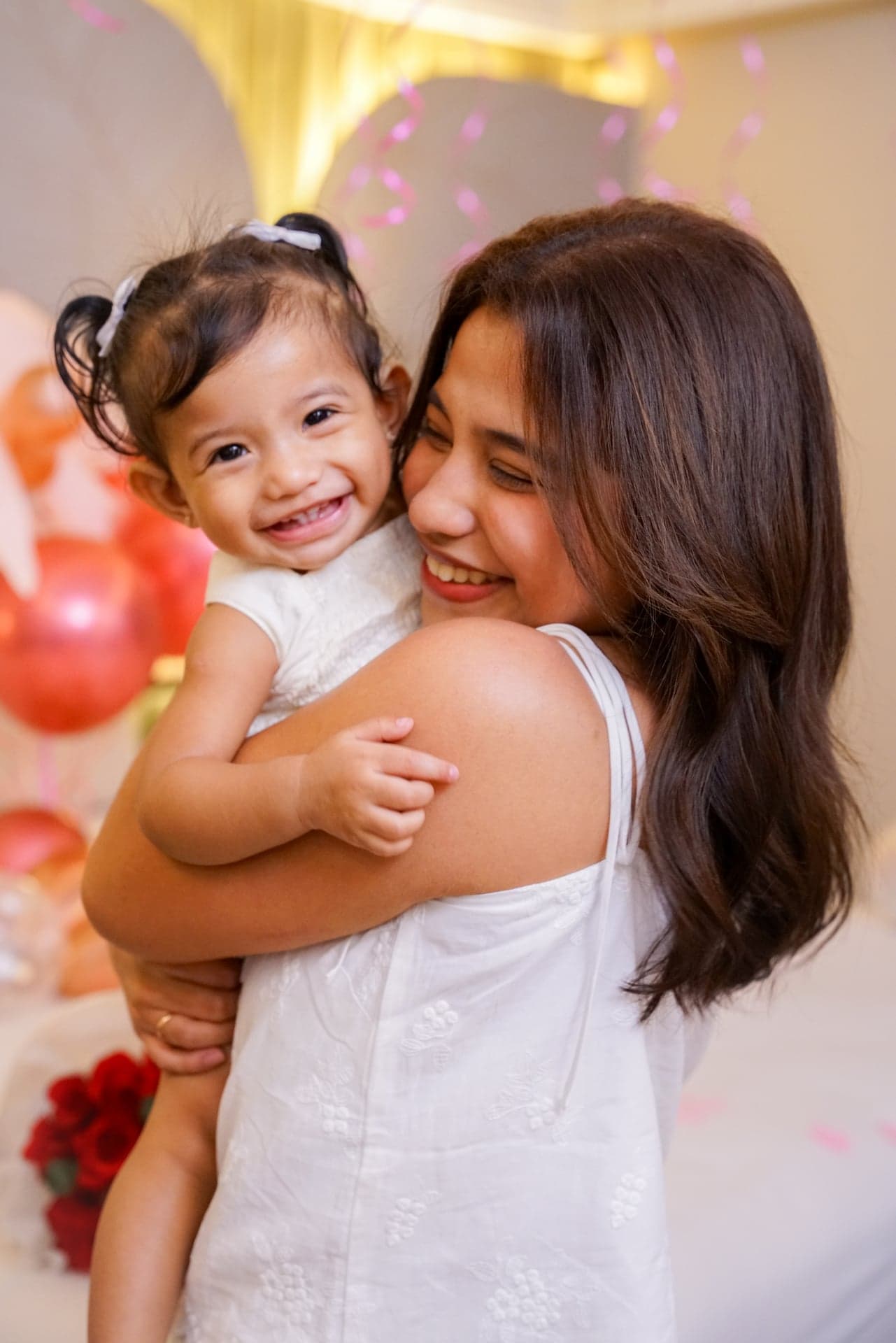 Woman holding a smiling child with balloon decorations behind them